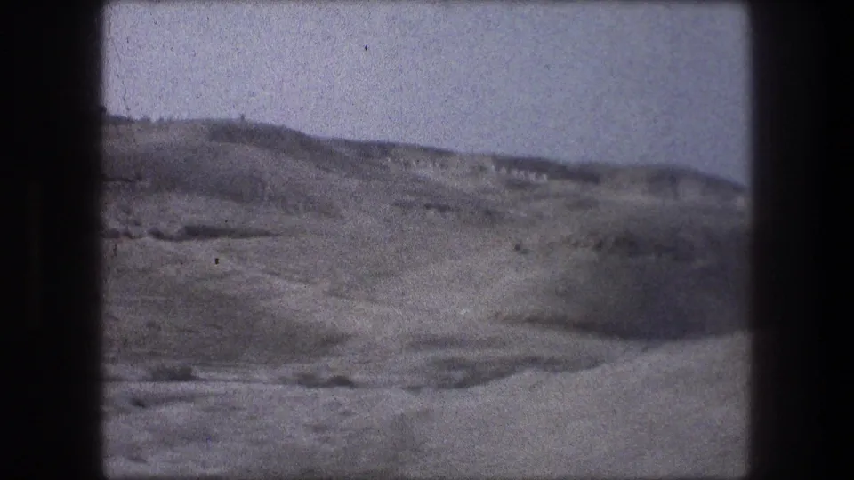 Soft 8mm frame from the Bethlehem-area landscape showing open dry terrain, low hills, and a hazy sky from a moving vehicle.