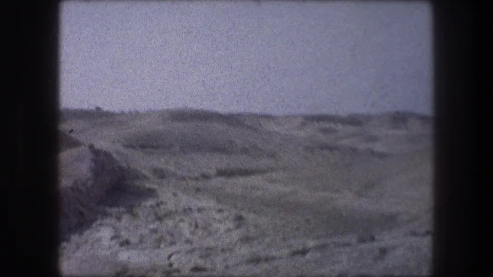 1976 8mm car-view frame near Bethlehem showing a rocky dirt track, sparse vegetation, and barren hills under a pale sky.