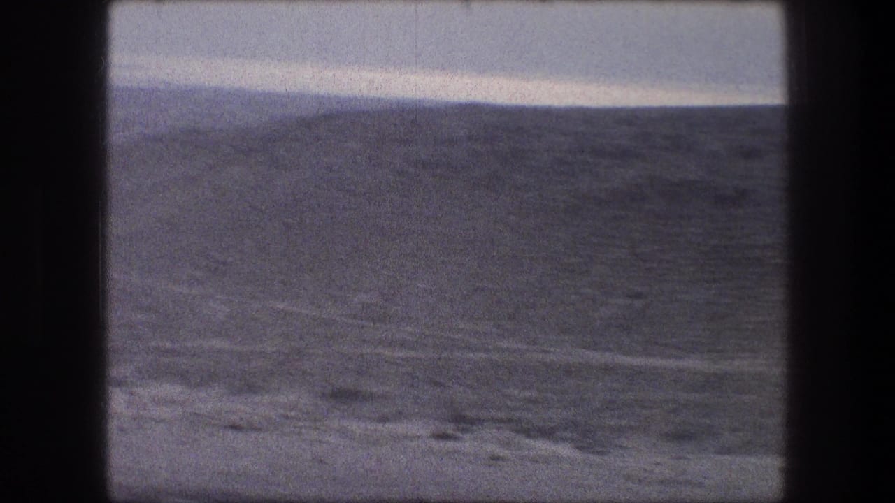 Wide hillside landscape with ridges and pale sky, framed by dark film borders.
