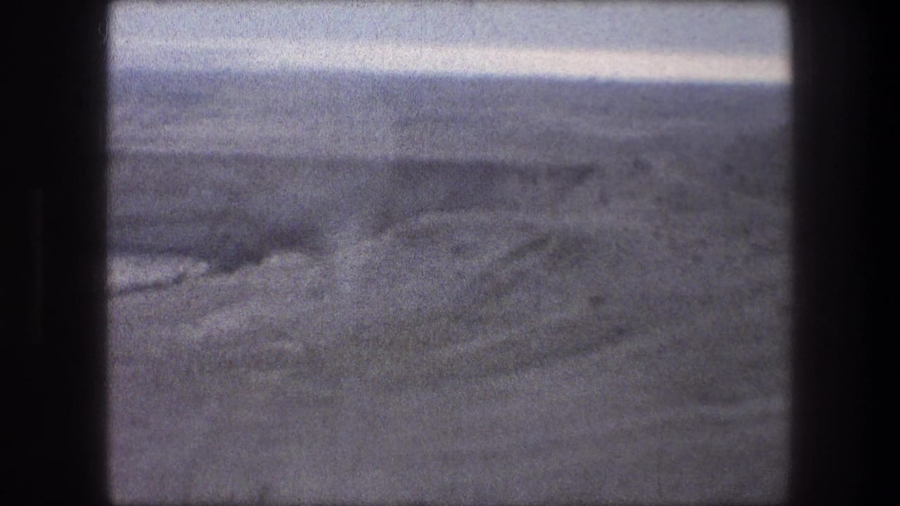 Barren open terrain seen through a dark vehicle window frame.
