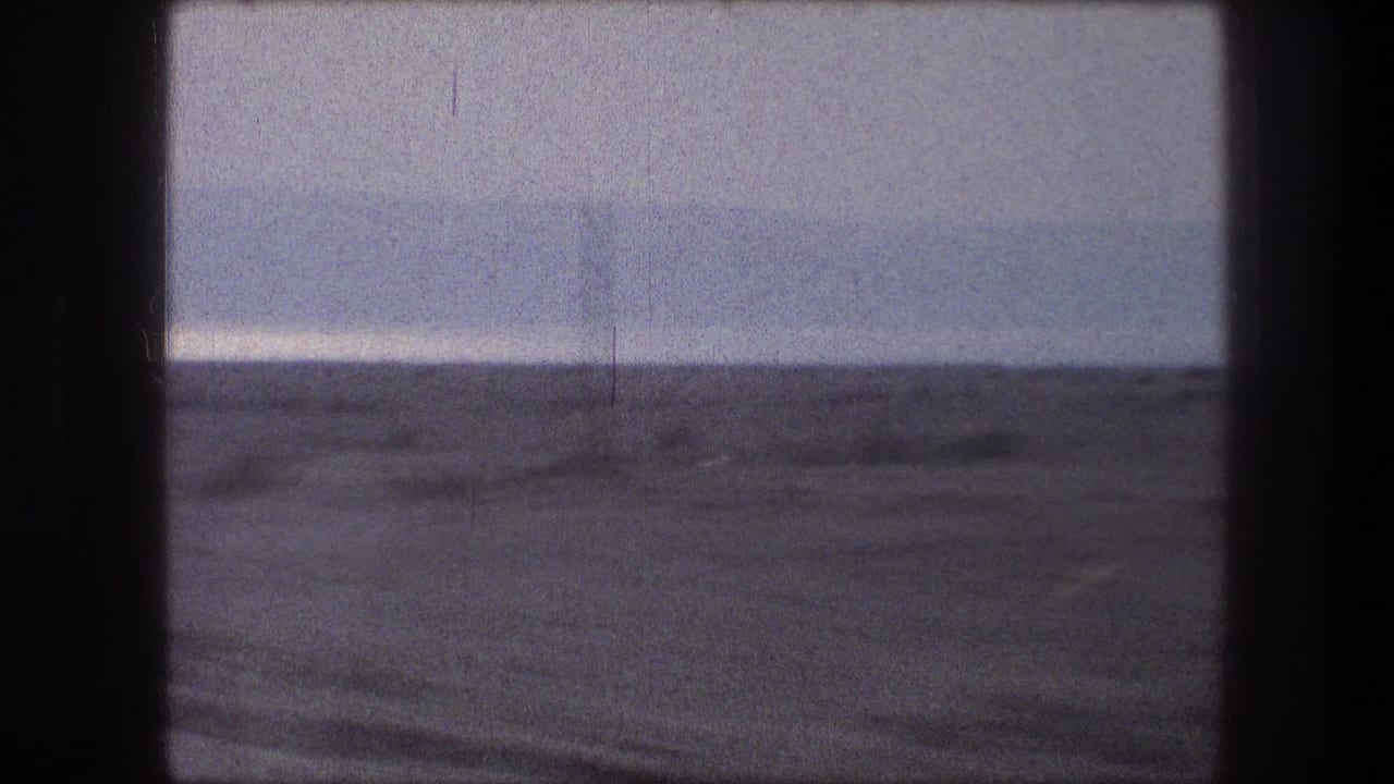 Arid landscape seen through a dark vehicle window frame under a hazy sky.