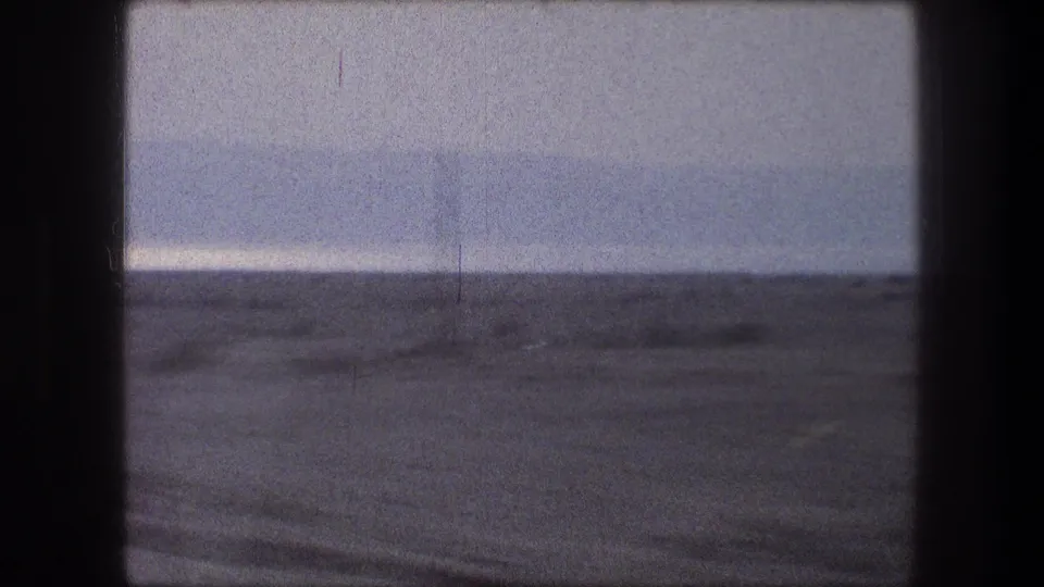 1976 Bethlehem-area 8mm view of flat desert terrain through a vehicle window, with a pale hazy sky and dark frame edges.