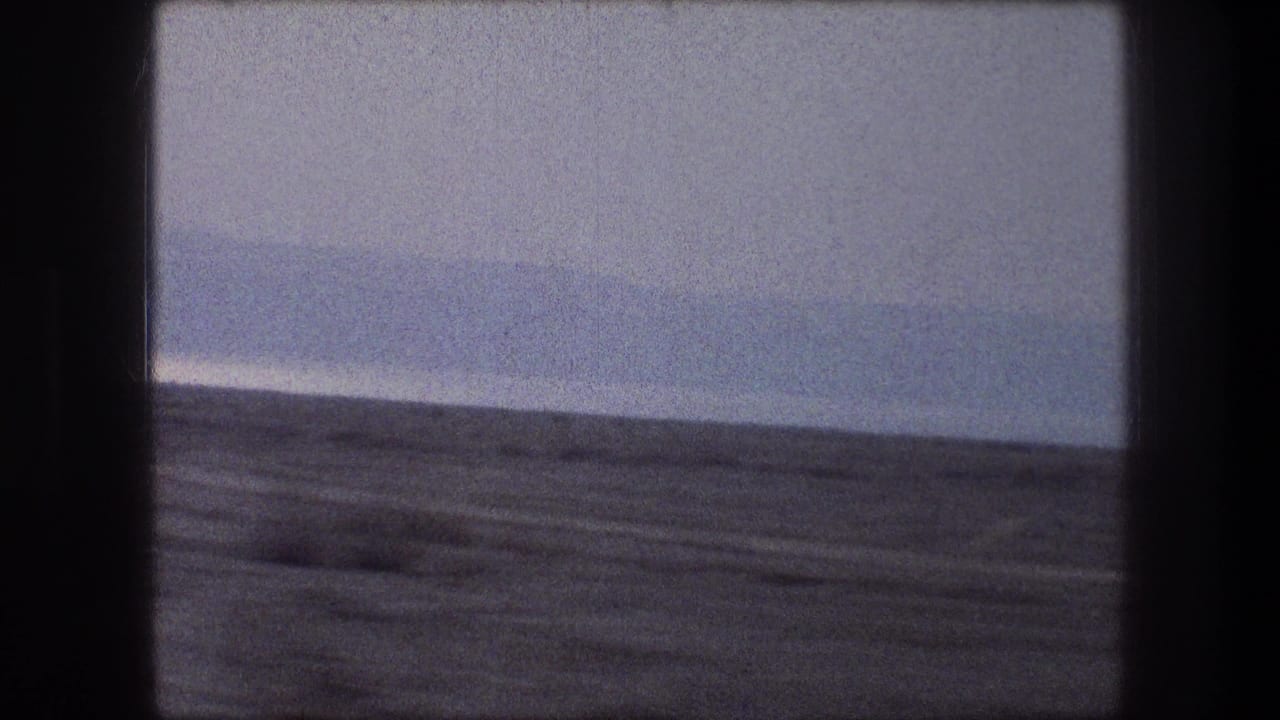 1976 Bethlehem-area roadside desert view from inside a vehicle, with muted color, grain, and a distant low horizon.