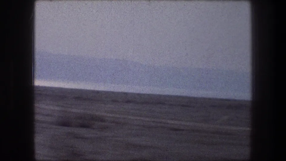 1976 Bethlehem-area roadside desert view from inside a vehicle, with muted color, grain, and a distant low horizon.