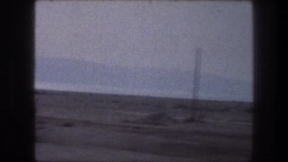 1976 Bethlehem-area 8mm frame showing arid roadside ground, a hazy sky, and a distant utility pole from a moving car.