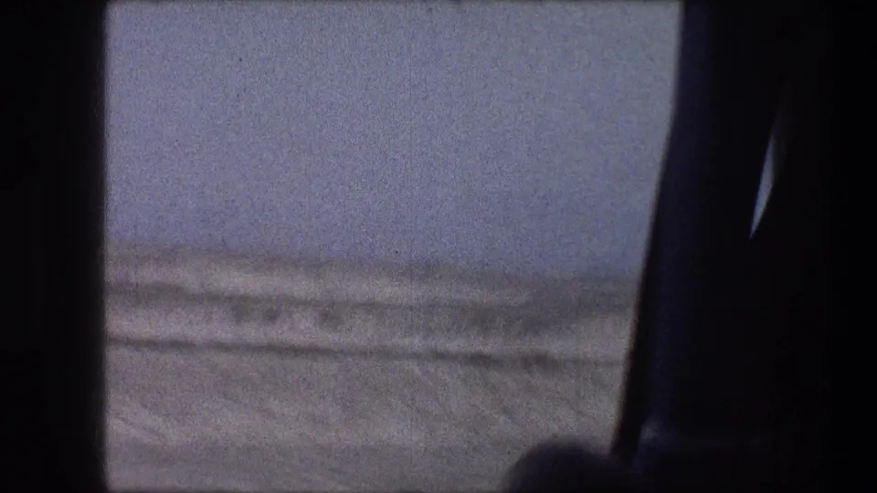 1976 8mm view near Bethlehem, Israel, looking past a dark car window toward pale snowy ground and a low horizon.