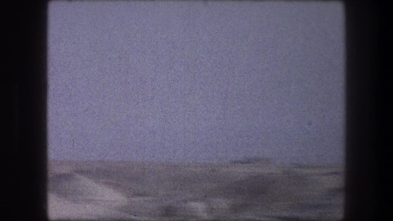 Hazy desert horizon with pale sky and sandy terrain seen through dark film gate edges.