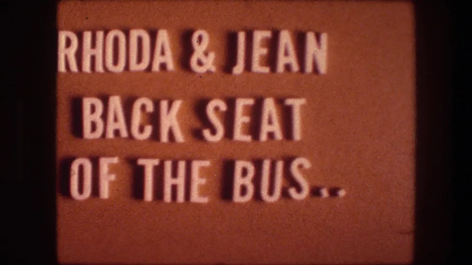 Orange 8mm title card with white text reading Rhoda and Jean back seat of the bus.