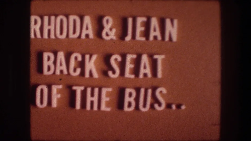 1976 8mm frame showing the orange home-movie title card for Rhoda and Jean, with the bus-seat wording still visible.