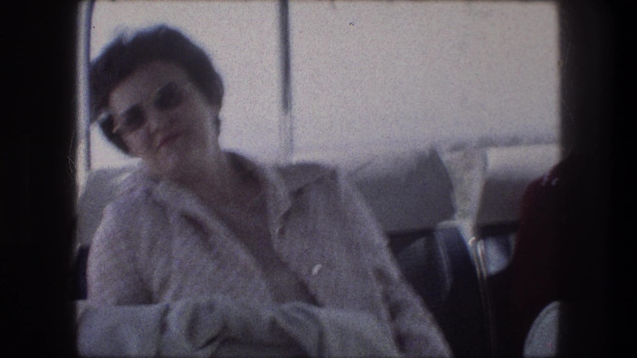 Woman in sunglasses rests inside a bus beside windows and blue curtains.
