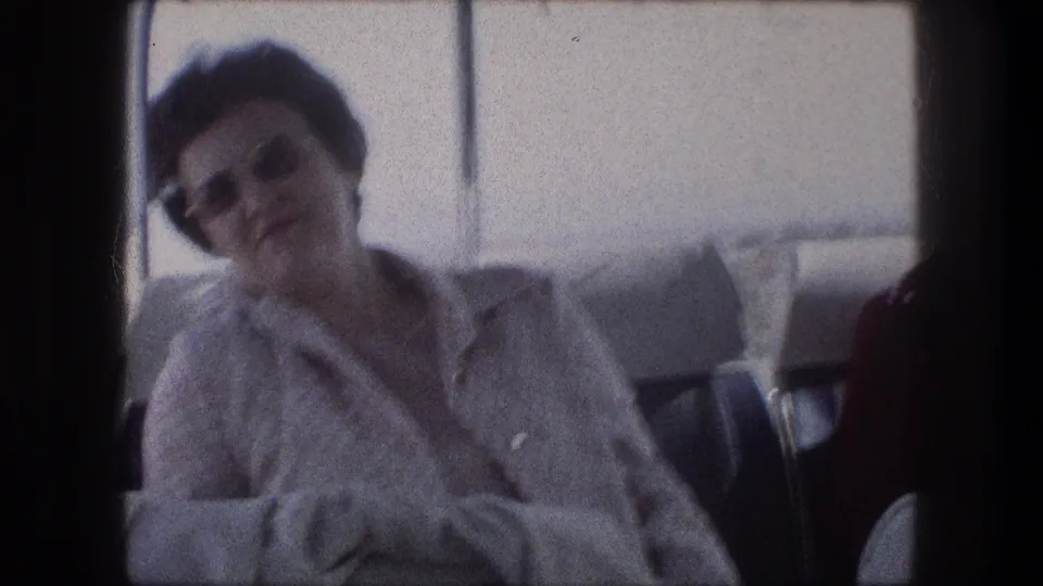 Adult woman in sunglasses sits inside a bus during 1976 travel near Bethlehem, Israel, with hazy landscape beyond the window.