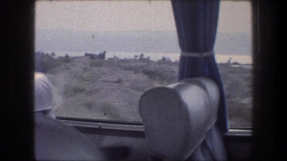 Bus interior detail from 1976 Bethlehem-area travel, with a seat back, tied blue curtain, and arid landscape outside.