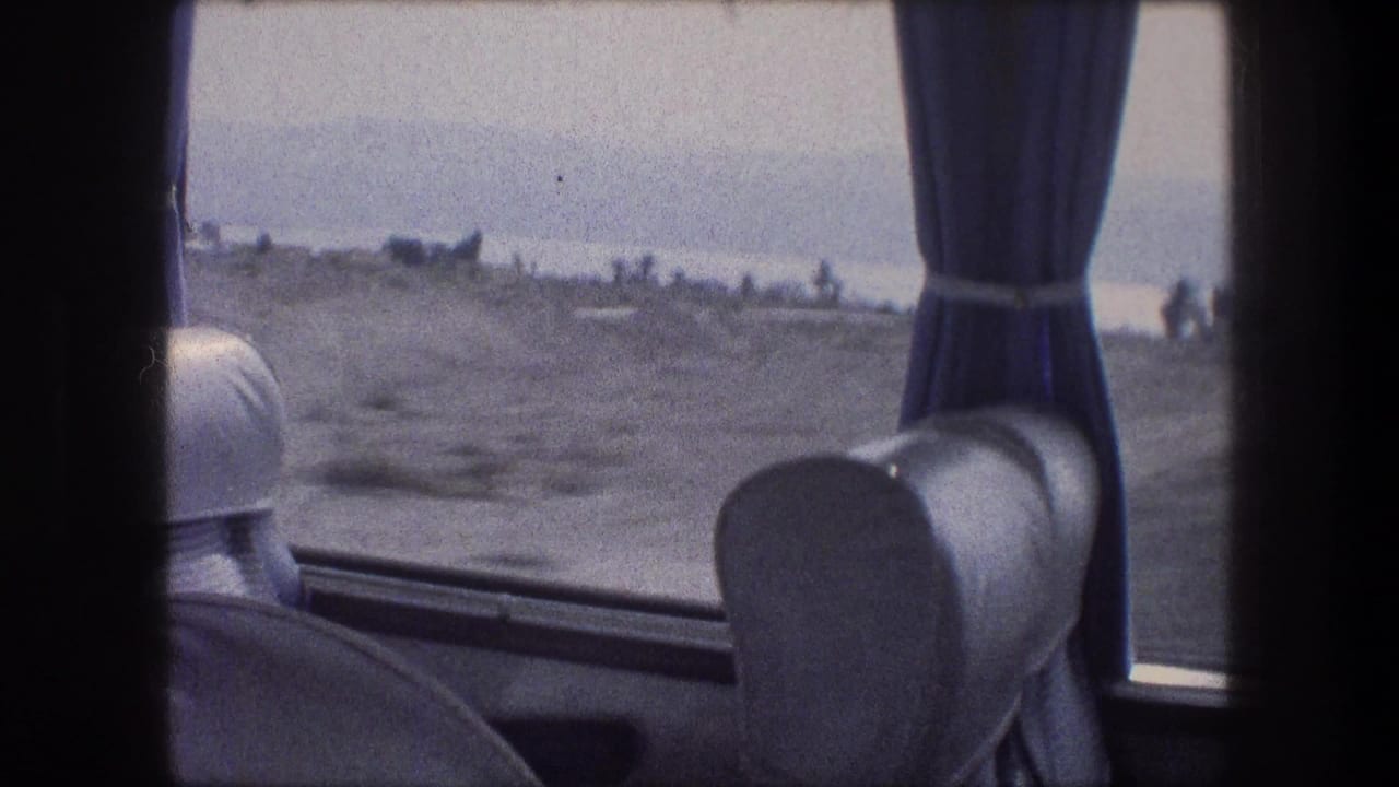 Seat backs and blue curtains frame a hazy roadside view from inside a moving vehicle.