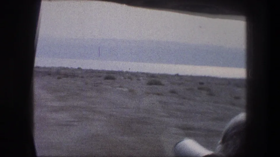 Bethlehem-area travel footage looking through a vehicle window at dry roadside terrain, sparse shrubs, and a pale distant horizon.