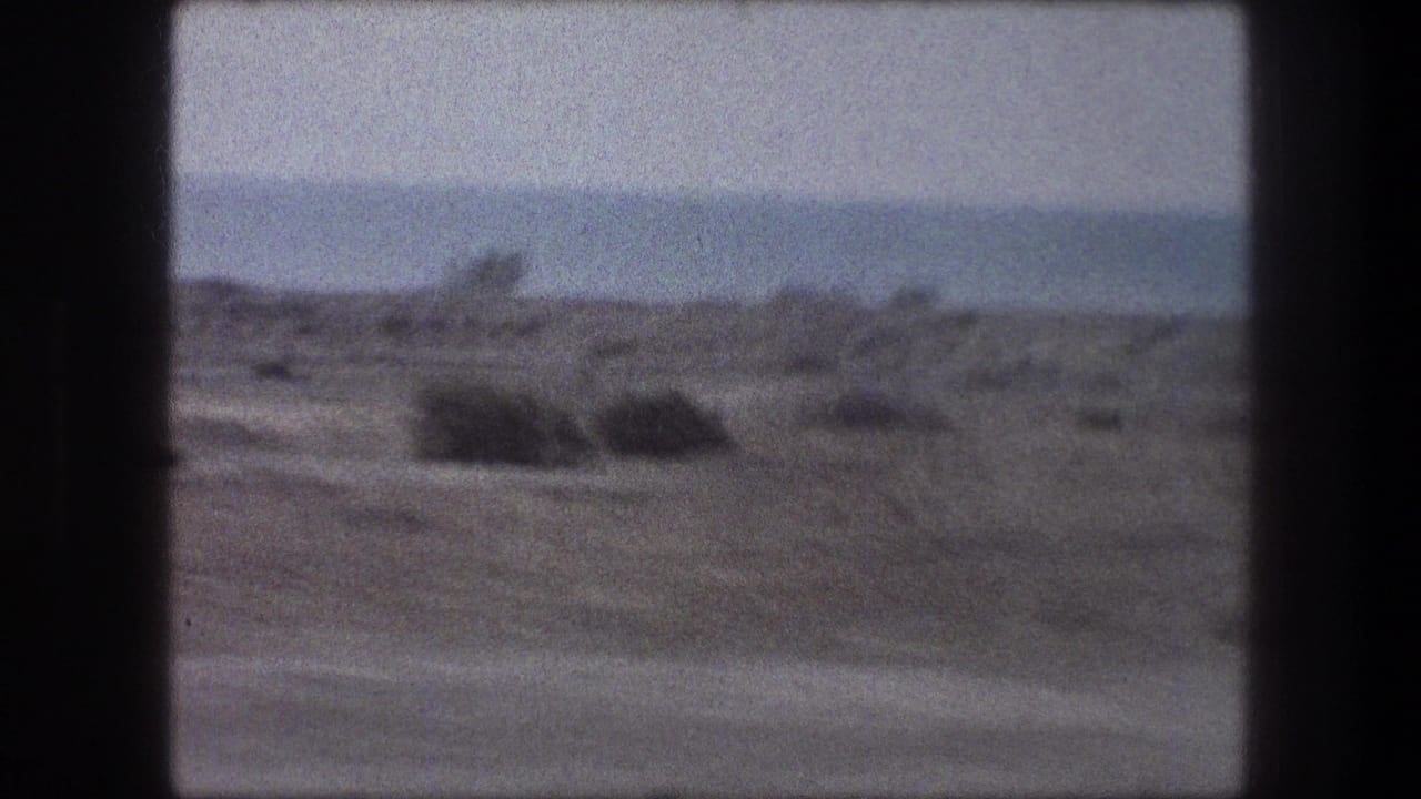 Passenger-window view of arid ground, scattered brush, and distant hills in 1976 8mm travel footage.