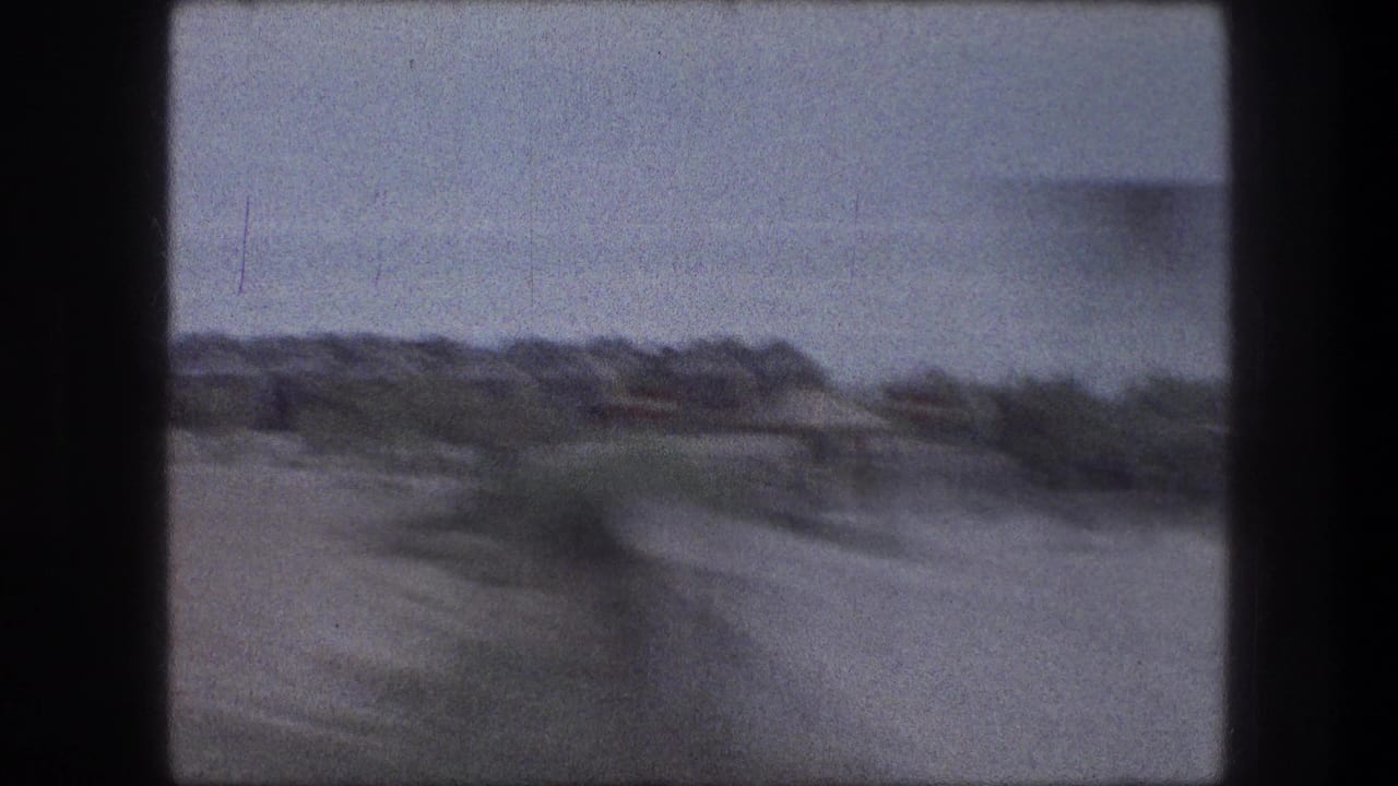 1976 8mm frame near Bethlehem showing a blurred field, scrub, pale sky, and distant low landscape from a moving vehicle.