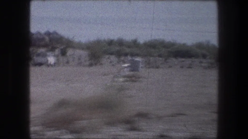 1976 8mm travel frame near Bethlehem with open ground, scrub vegetation, and indistinct distant buildings or hills.