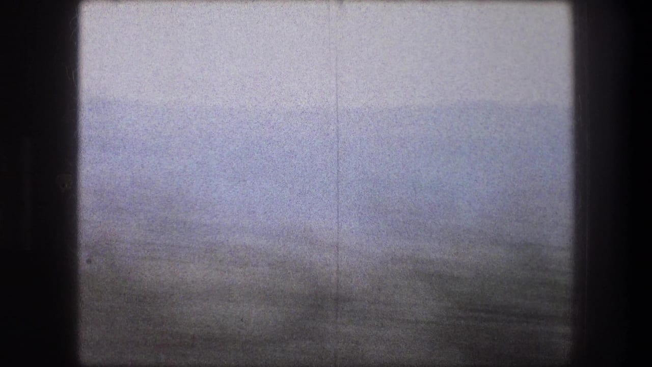 1976 8mm frame from Bethlehem, Israel, showing a soft, blurred landscape with dark vegetation and a pale sky.