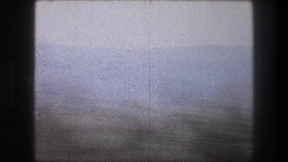 1976 8mm frame from Bethlehem, Israel, showing a soft, blurred landscape with dark vegetation and a pale sky.