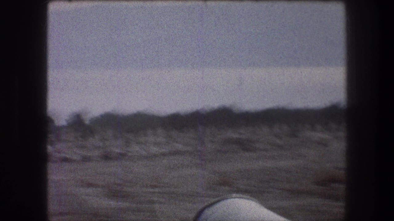1976 Bethlehem-area travel frame with dry open ground, distant low shrubs, pale sky, and soft 8mm motion blur.