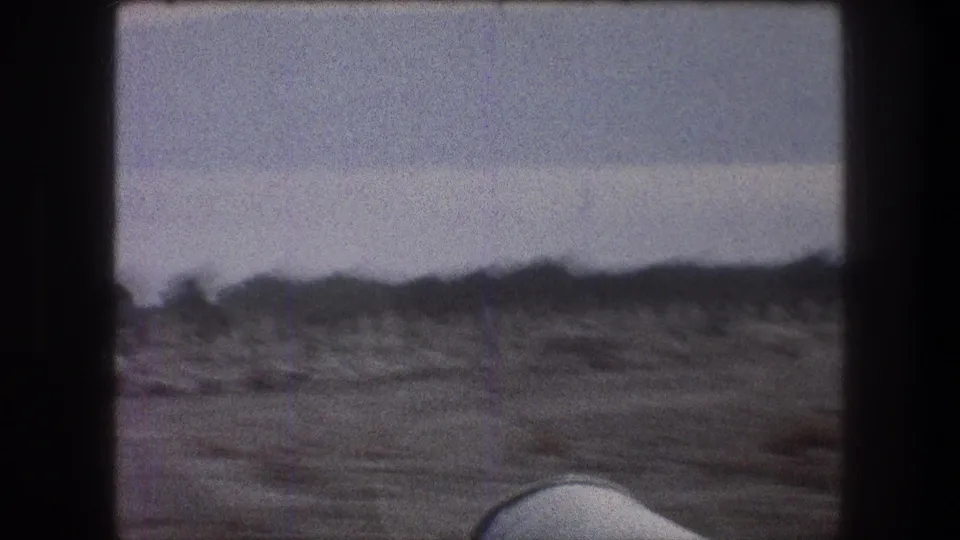 1976 Bethlehem-area travel frame with dry open ground, distant low shrubs, pale sky, and soft 8mm motion blur.