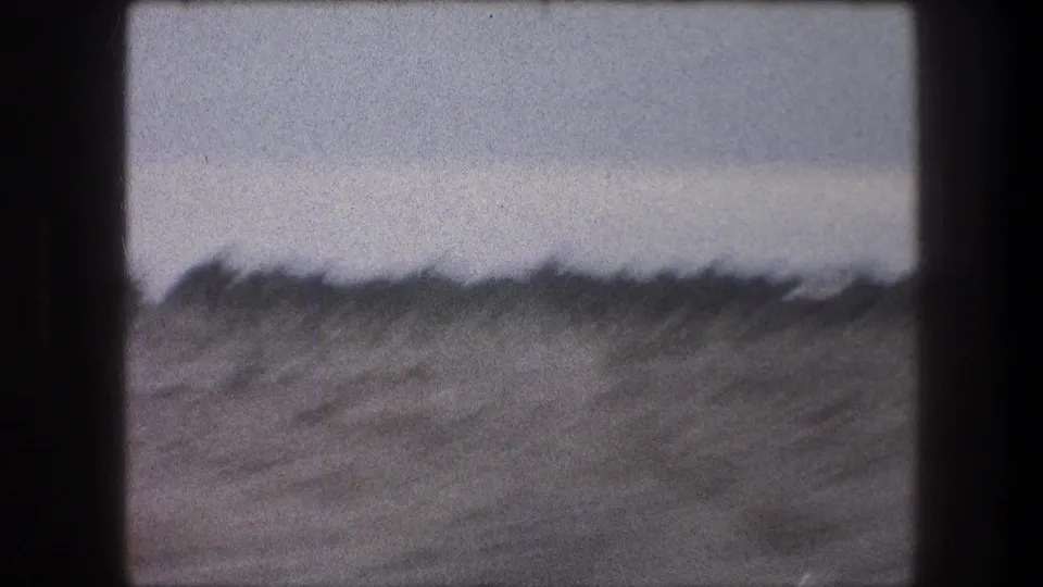 1976 Bethlehem-area home-movie frame showing a dry field, low vegetation, muted sky, grain, and dark frame edges.