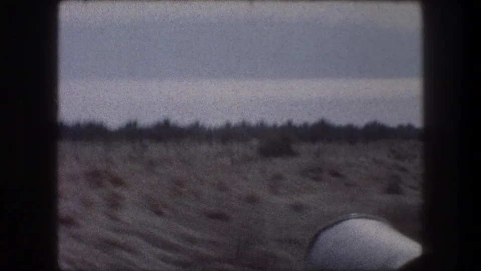 1976 8mm view near Bethlehem showing arid scrub terrain through a car window, with hazy sky and a white vehicle part visible.