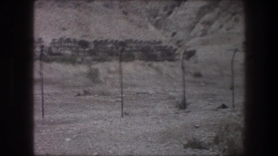 1976 8mm view near Bethlehem showing a blurred fence line, sandy ground, brush and a rocky hillside through the home-movie frame.