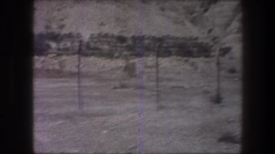 1976 Bethlehem-area 8mm frame of fence posts, scrub, sandy terrain and a rocky hillside, bordered by the dark film frame.
