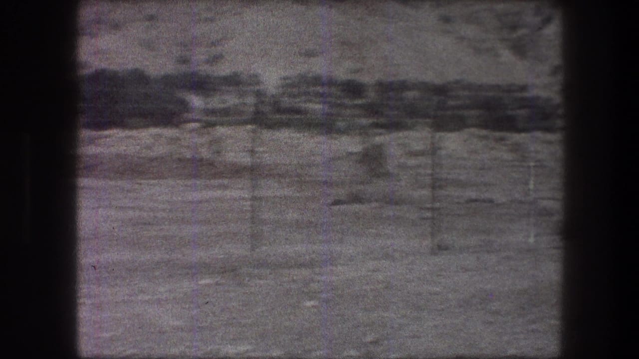 1976 8mm view of a barren Bethlehem-area landscape, partially obscured by dark framing, with faint utility lines and hillside beyond.