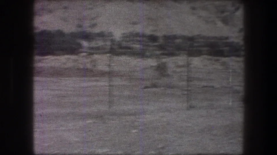 1976 8mm view of a barren Bethlehem-area landscape, partially obscured by dark framing, with faint utility lines and hillside beyond.
