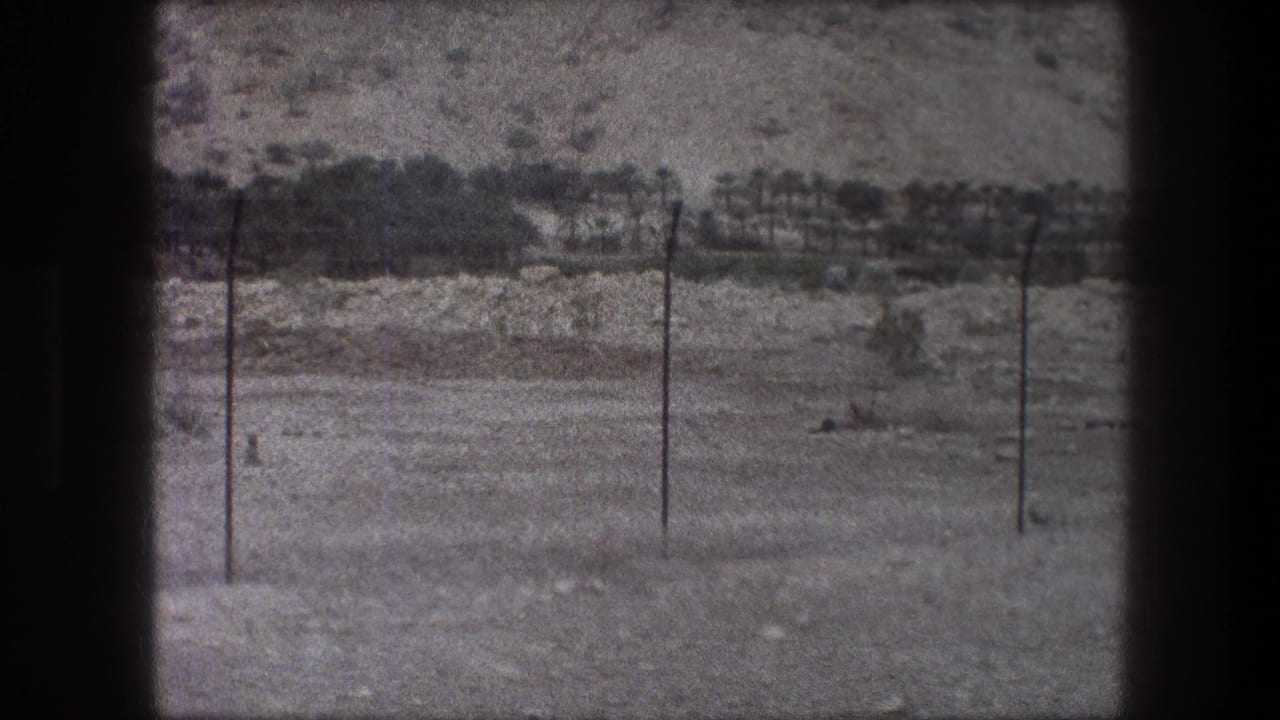 Two utility poles stand in rocky open terrain with a low hillside and sparse brush behind them.