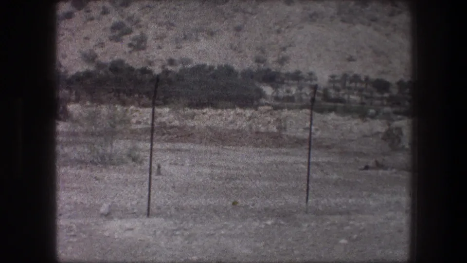 1976 8mm Bethlehem landscape with utility poles in the foreground, dry open ground, and a rocky slope with sparse trees beyond.