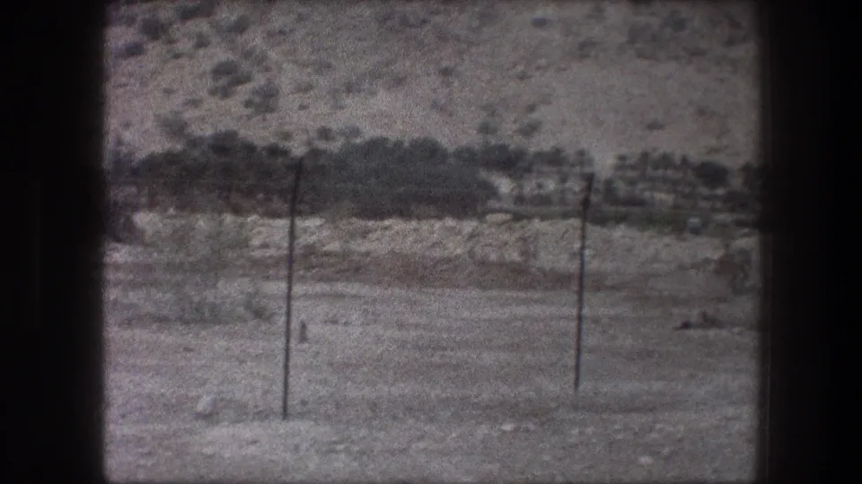 Bethlehem, Israel, 1976: muted 8mm frame of utility poles and faint wires set against dry terrain and a scrub-covered hillside.