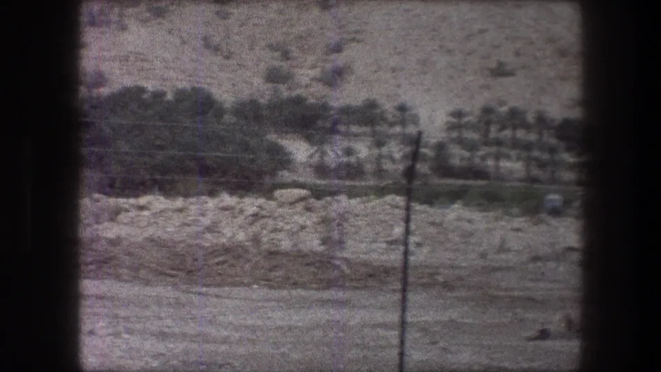 1976 8mm Bethlehem-area landscape showing rocky ground, a low band of greenery, and a foreground fence post.