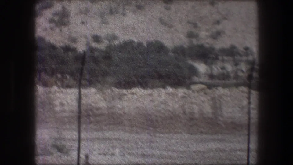1976 Bethlehem home-movie frame showing a rocky, scrub-covered hillside beyond a dark window frame and simple fencing.