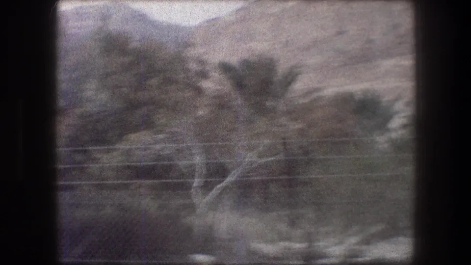 1976 8mm view near Bethlehem showing a blurred rocky hillside, scrub vegetation, and power lines from a moving vehicle.