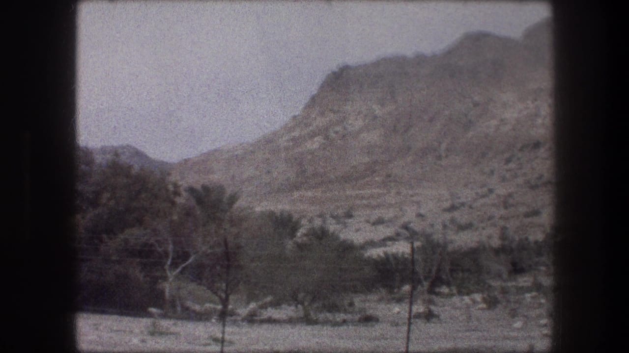 Tan hillside beyond scattered trees and dry ground, framed by black film borders.
