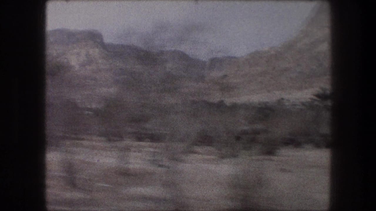 Dry hills and sparse roadside vegetation seen through dark film-frame borders.