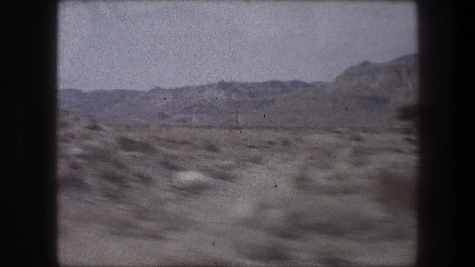 Late-frame 1976 8mm view near Bethlehem, Israel, with open scrubland, pale desert tracks, and a low mountain range on the horizon.