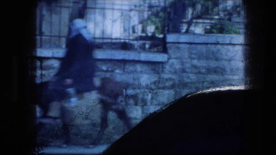 1976 Garden Tomb area frame with a blurred distant figure and horse moving past stone walls and railings, partly obscured by dark film edge.