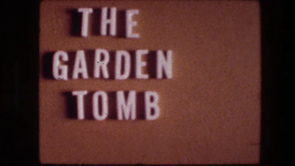 A wider 8mm frame shows the Garden Tomb sign lettering on a brown plaque or wall, recorded from a visitor viewpoint.