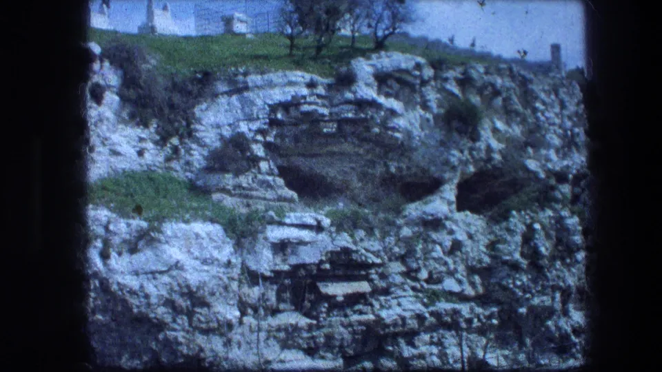 Vintage 1976 Jerusalem travel frame showing the Garden Tomb hillside with limestone strata, grass, sparse trees, and a white structure above.