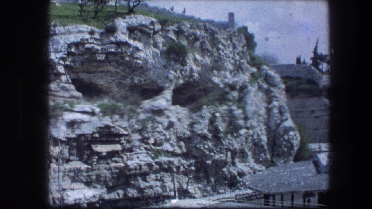 Rugged limestone cliff with dark cave openings and grass above.