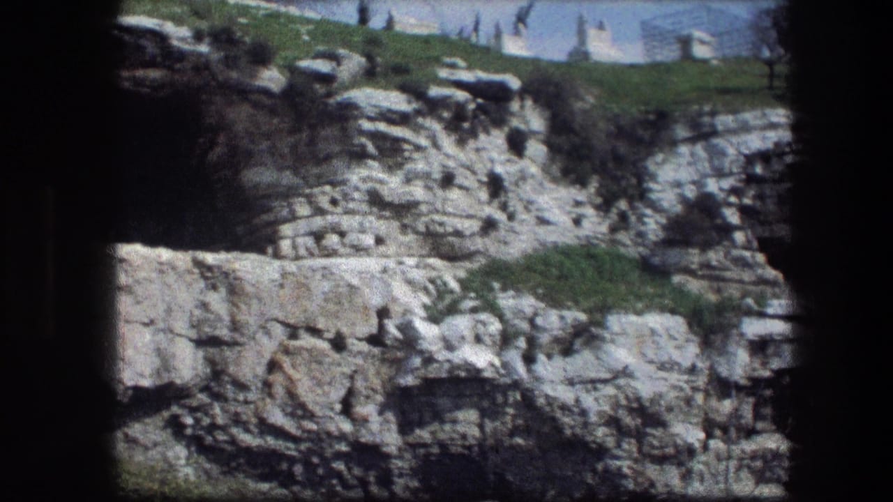 Rocky limestone cliff with cave recesses, grass at top, and dark film border.