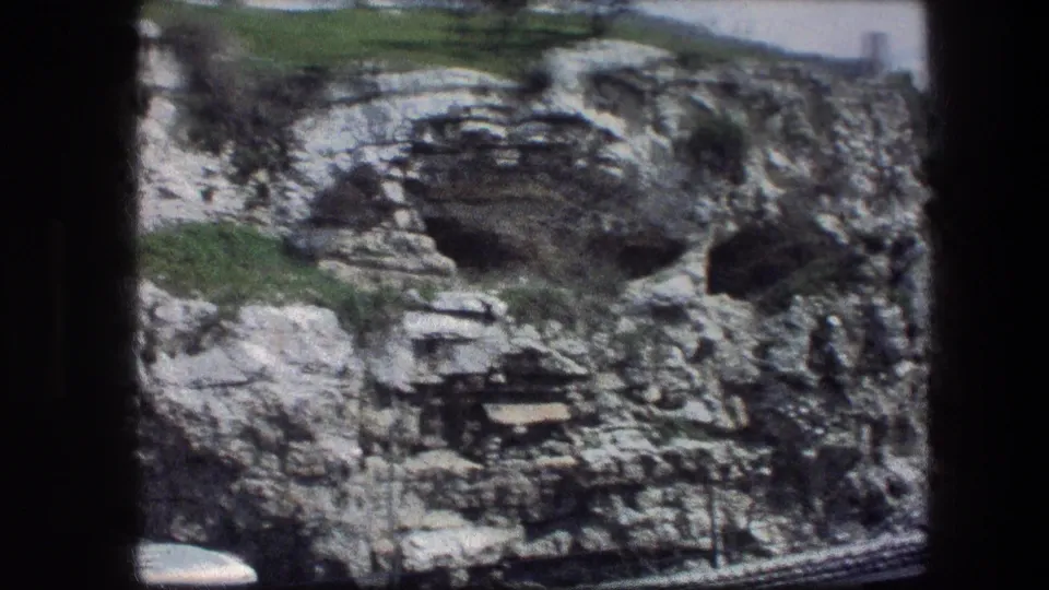 Garden Tomb rock face in Jerusalem, captured on 8mm in 1976, with an arched recess, small cave opening, grass, and soft film edges.