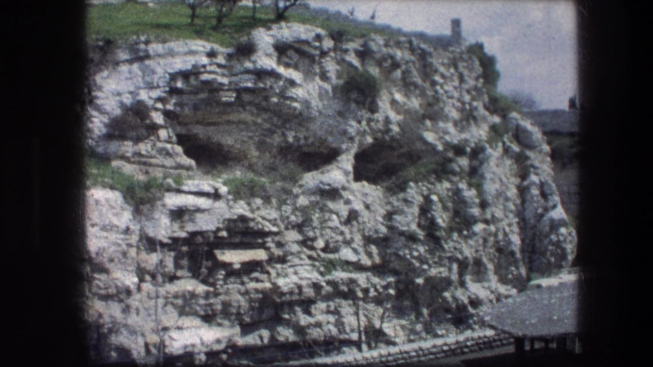 Rocky limestone hillside with cave-like openings and sparse greenery.