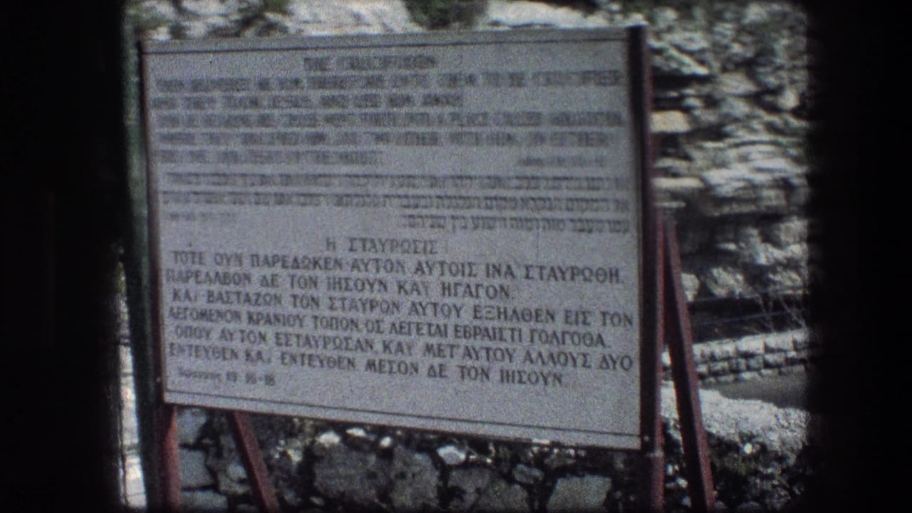 Multilingual crucifixion sign on a metal frame before a stone wall.