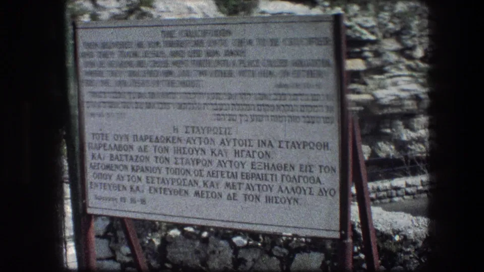 1976 8mm frame of a Garden Tomb sign in Jerusalem with English, Hebrew, and Greek text about the crucifixion.