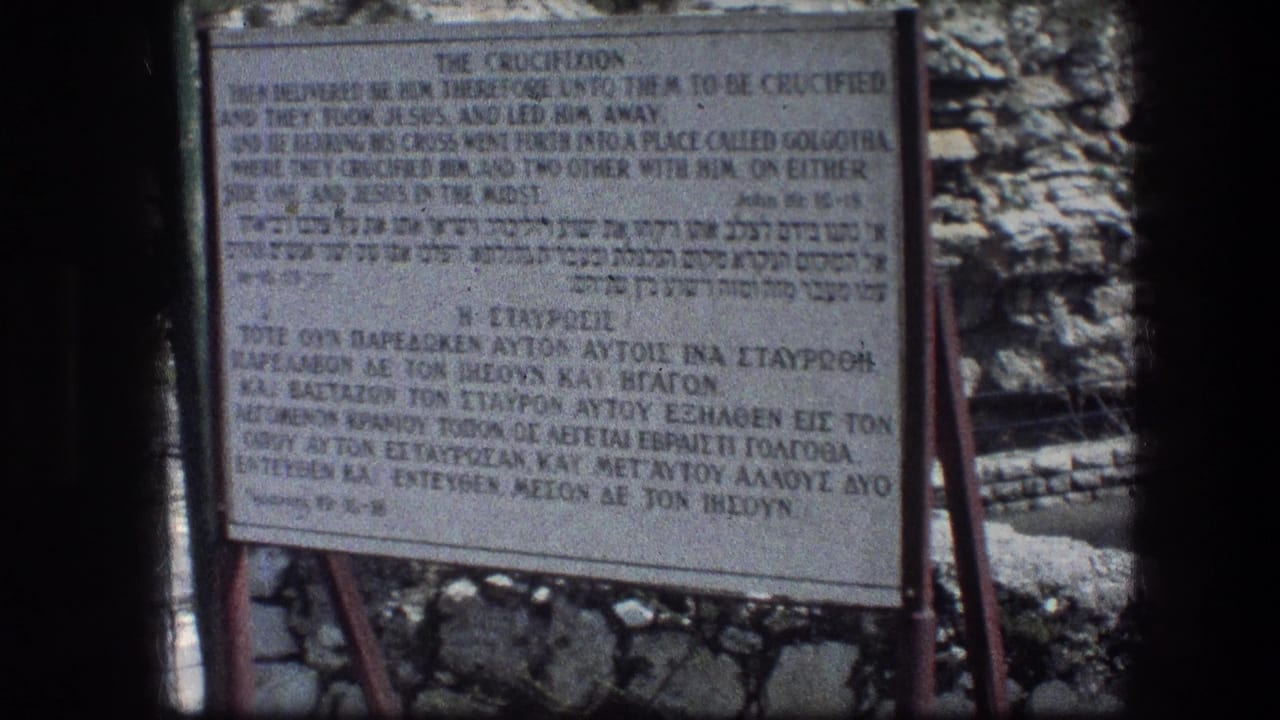 Crucifixion sign with English, Hebrew, and Greek text beside rough stonework.